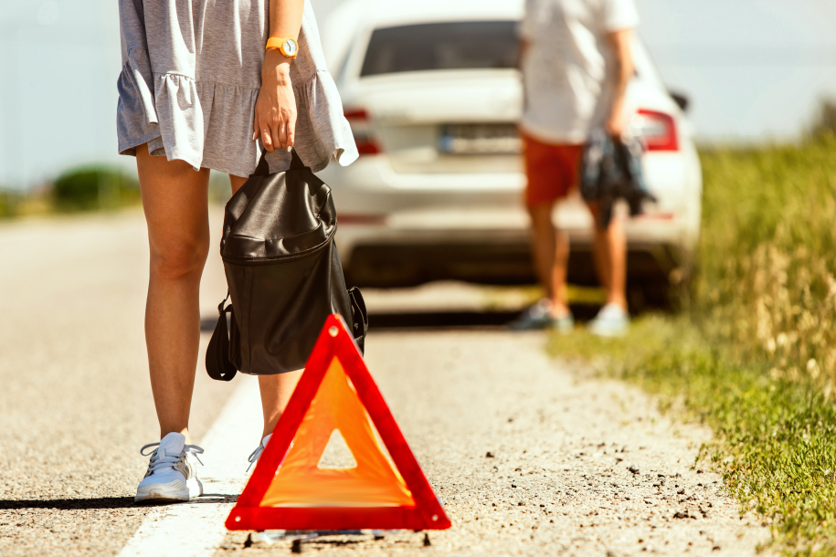 The young couple broke down the car while traveling on the way to rest. They are trying to stop other drivers and ask for help or hitchhike. Relationship, troubles on the road, vacation.